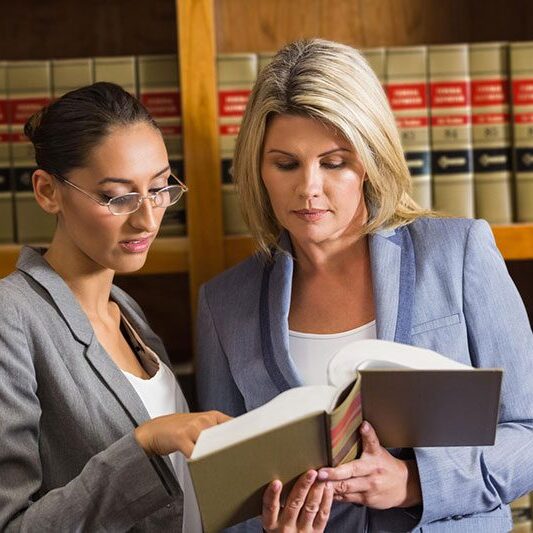 Two women in a law office looking at books.